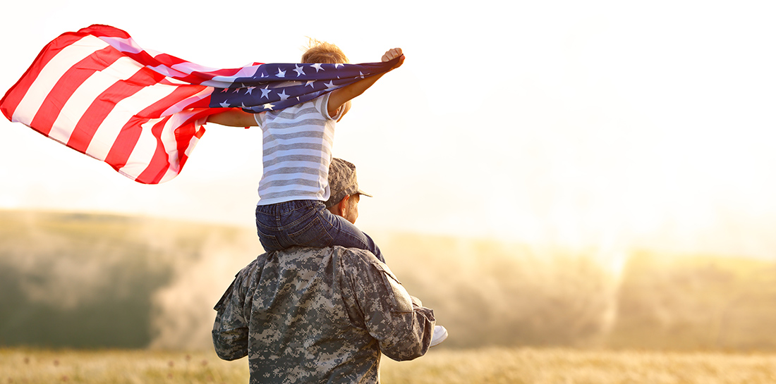 Rear view of military man father carrying happy little son with american flag on shoulders and enjoying amazing summer nature view on sunny day, happy male soldier dad reunited with son after US army